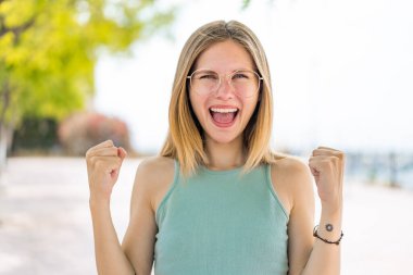 Genç sarışın kadın açık havada gözlüklü ve zaferi kutluyor.