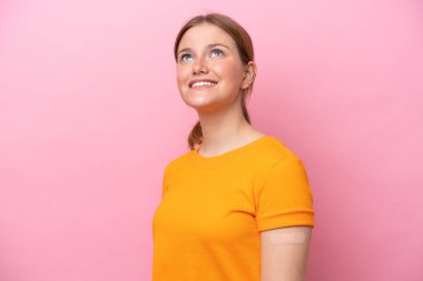 Young caucasian woman wearing band aid isolated on pink background looking up while smiling