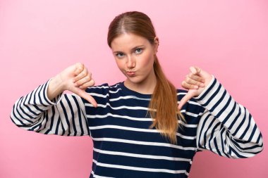 Pembe arka planda izole edilmiş beyaz bir kadın baş parmağını iki eliyle aşağı gösteriyor.