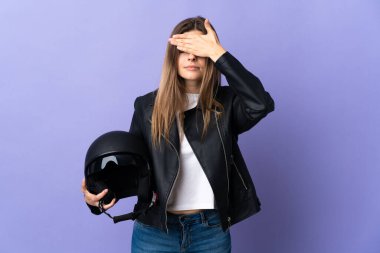 Young slovak woman holding a motorcycle helmet isolated on purple background covering eyes by hands. Do not want to see something