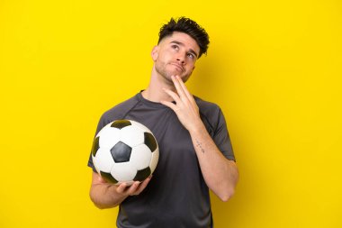 Yakışıklı genç futbolcu sarı arka planda izole edilmiş gülümserken yukarı bakıyor.