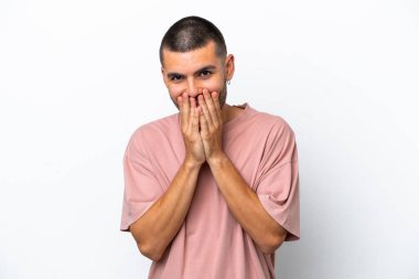 Beyaz arka planda izole edilmiş genç beyaz bir adam mutlu ve gülümseyen elleriyle ağzını kapatıyor.