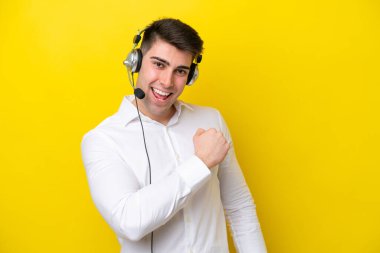 Tele pazarlamacı beyaz adam sarı arka planda izole edilmiş bir kulaklıkla çalışarak zaferi kutluyor.