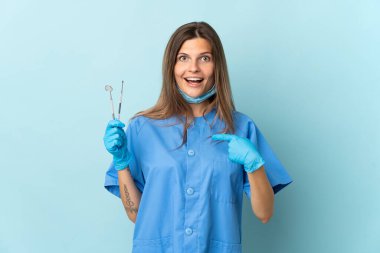 Slovak diş hekimi mavi arkaplanda sürpriz yüz ifadesi ile izole araçlar tutuyor