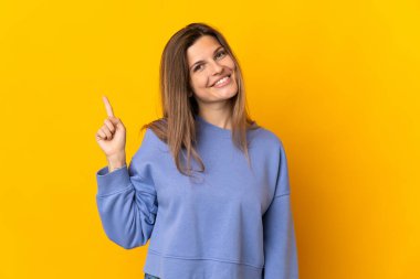 Genç Slovak kadın sarı arka planda izole edilmiş ve en iyinin işareti olarak parmağını kaldırıyor.