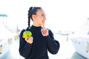 Açık havada elmalı genç Faslı kız bir fikir üretiyor ve bakıyor.