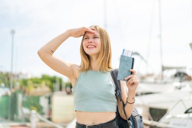 Açık havada genç sarışın bir kadın elinde pasaport, şaşırmış bir ifadeyle.