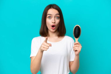 Mavi arka planda saç tarağı olan genç Ukraynalı kadın şaşırmış ve ön tarafı işaret ediyor.