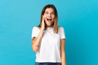 Genç Slovak kadın mavi arka planda izole edilmiş, şaşırmış ve şok olmuş bir yüz ifadesi var.