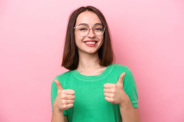 Genç Ukraynalı kadın pembe arka planda izole edilmiş gözlüklü ve başparmağıyla
