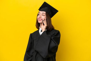 Genç üniversite mezunu Ukraynalı bir kadın sarı arka planda izole edilmiş cep telefonuyla biriyle sohbet ediyor.