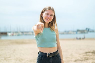 Açık havadaki genç sarışın kadın kendine güvenen bir ifadeyle seni işaret ediyor.