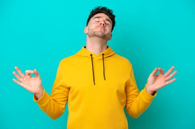 Zen pozisyonunda mavi arka planda izole edilmiş genç beyaz bir adam.