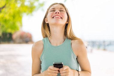 Açık havada cep telefonu kullanan genç sarışın bir kadın.
