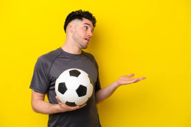 Yakışıklı genç futbolcu, sarı arka planda yalıtılmış, sürpriz bir ifadeyle yan tarafa bakarken.