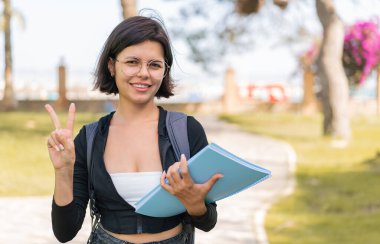Açık havada gülümseyen ve zafer işareti gösteren genç Bulgar öğrenci kadın.