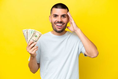 Kafkasyalı genç bir adam, sarı arka planda, sürpriz bir ifadeyle izole edilmiş bir sürü para alıyor.