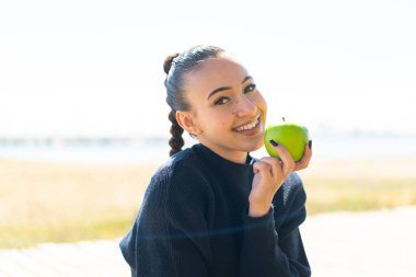 Genç Faslı kız açık havada elinde mutlu bir ifadeyle bir elma tutuyor.