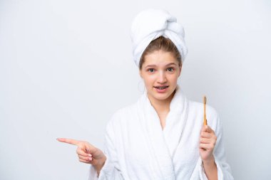 Beyaz arka planda izole edilmiş dişlerini fırçalayan genç Rus kız şaşırmış ve parmağını kenarı işaret ediyor.