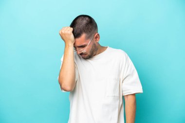 Kafkasyalı genç adam mavi arka planda izole edilmiş, baş ağrısı var.