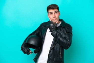 Motosiklet kasklı genç beyaz adam mavi arka planda izole edilmiş. Şüpheleri var.