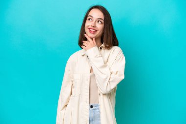 Genç Ukraynalı kadın mavi arka planda izole edilmiş gülümserken yukarı bakıyor