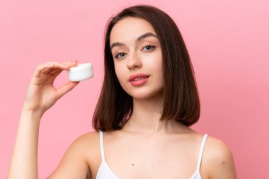 Genç Ukraynalı kadın pembe arka planda nemlendirici ile izole edilmiş.