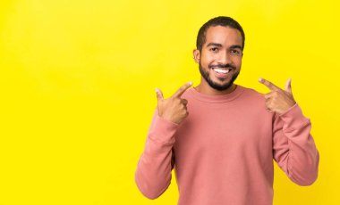 Sarı arka planda izole edilmiş genç latin adam baş parmak işareti yapıyor.