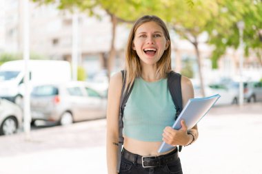 Sarışın genç bayan şaşkınlık ve şok olmuş yüz ifadesiyle dışarıda.