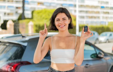 Genç, güzel, Bulgar bir kadın elinde araba anahtarı tutarak harika bir fikri işaret ediyor.