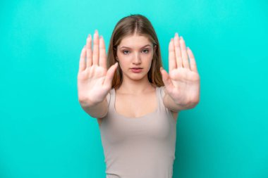 Genç Rus kız mavi arka planda izole edilmiş. Durma hareketi yapıyor ve hayal kırıklığına uğruyor.