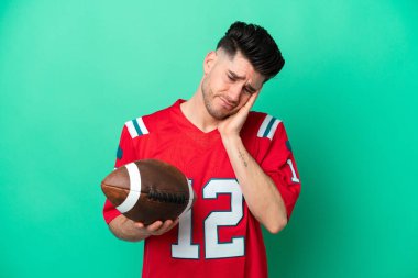 Rugby oynayan beyaz bir adam yeşil arka planda baş ağrısı ile izole edilmiş.