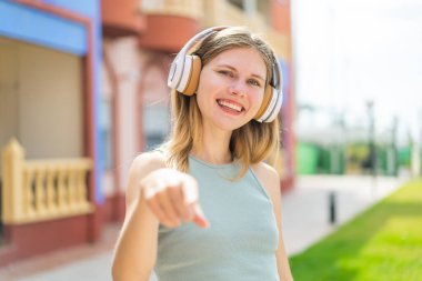 Açık havada müzik dinleyen genç sarışın kadın.