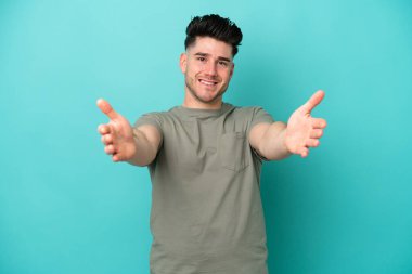 Mavi arka planda izole edilmiş genç beyaz adam sunar ve davet eder.