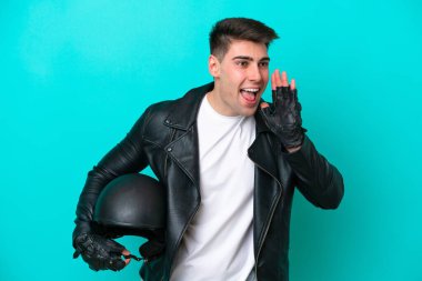 Motosiklet kasklı genç beyaz adam mavi arka planda izole edilmiş ağzı sonuna kadar açık bağırıyor.