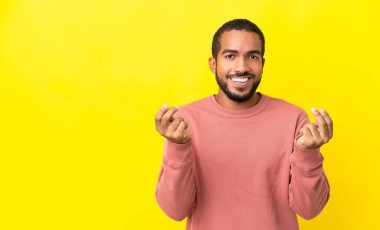 Sarı arka planda izole edilmiş genç Latin adam para hareketi yapıyor.