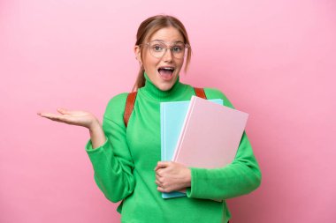 Yüzünde şok ifadesi olan, pembe arka planda izole edilmiş beyaz bir kadın öğrenci.