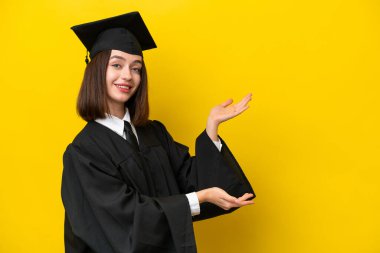 Genç üniversite mezunu Ukraynalı bir kadın sarı arka planda izole edilmiş ve davet edilmek için ellerini yana uzatıyor.