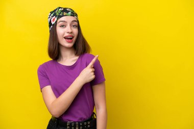 Sarı arka planda izole edilmiş genç Ukraynalı kadın şaşırmış ve işaret ediyor.