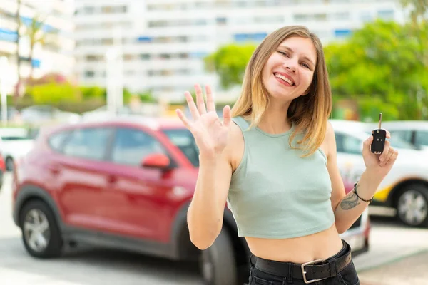 Dışarıda arabanın anahtarlarını tutan genç sarışın kadın mutlu bir ifadeyle selamlıyor.