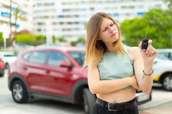 Genç sarışın kadın dışarıda arabanın anahtarlarını tutuyor, üzgün bir ifadeyle.
