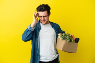 Rus adam sarı arka planda izole edilmiş, baş ağrısı olan şeylerle dolu bir kutuyu kaldırırken hamle yapıyor.