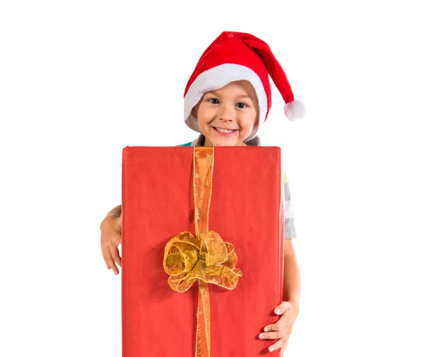 Kid with christmas hat holding a big red gift — Stock Photo, Image