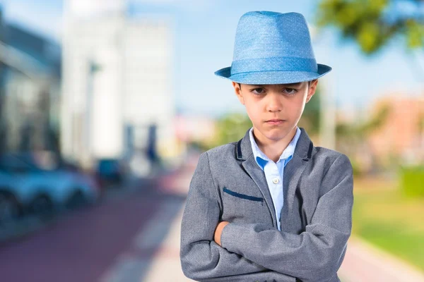 Criança triste com os braços cruzados usando um chapéu azul — Fotografia de Stock