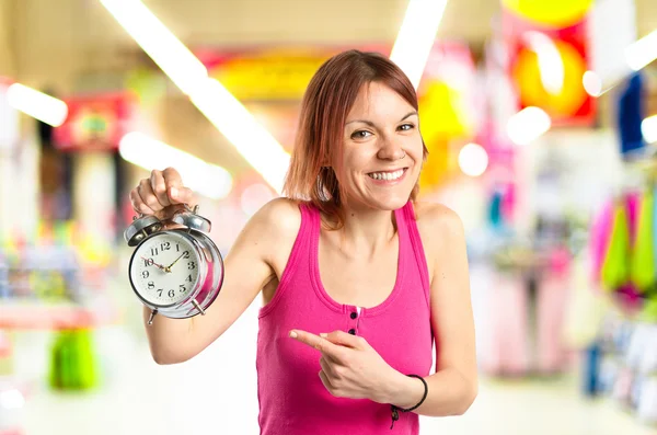 Glücklich rothaarige Mädchen hält eine Uhr über weißem Hintergrund — Stockfoto