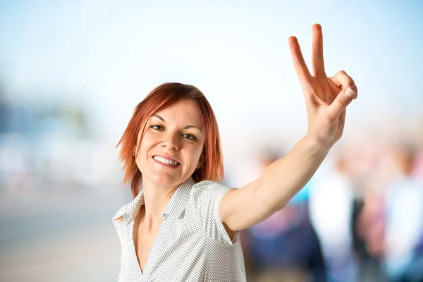 Junge Frau macht Siegesgeste vor weißem Hintergrund — Stockfoto