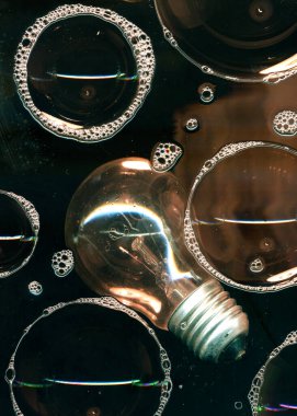 Cam yüzeyde siyah arkaplanda izole edilmiş ampul ve sabun köpükleri. Karanlıkta ışık. Fikir ampulü soyut aydınlatma dekorasyonu. Lamba ampul konsepti resmi.