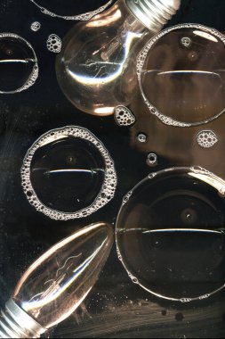 Cam yüzeyde siyah arkaplanda izole edilmiş ampul ve sabun köpükleri. Karanlıkta ışık. Fikir ampulü soyut aydınlatma dekorasyonu. Lamba ampul konsepti resmi.