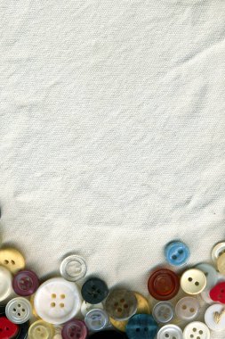 Kumaş dokusu arka planında renk düğmeleri çerçevesi dikiliyor. Çeşitli yedek kıyafet düğmeleri koleksiyonu eski. Dikiş araçları kapatılıyor. 