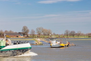 Gelderland eyaletindeki sel basmış IJssel nehri üzerinde bir feribottan geçen kargo gemisi
